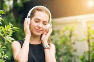 woman listening to white headphones in garden with sun flare
