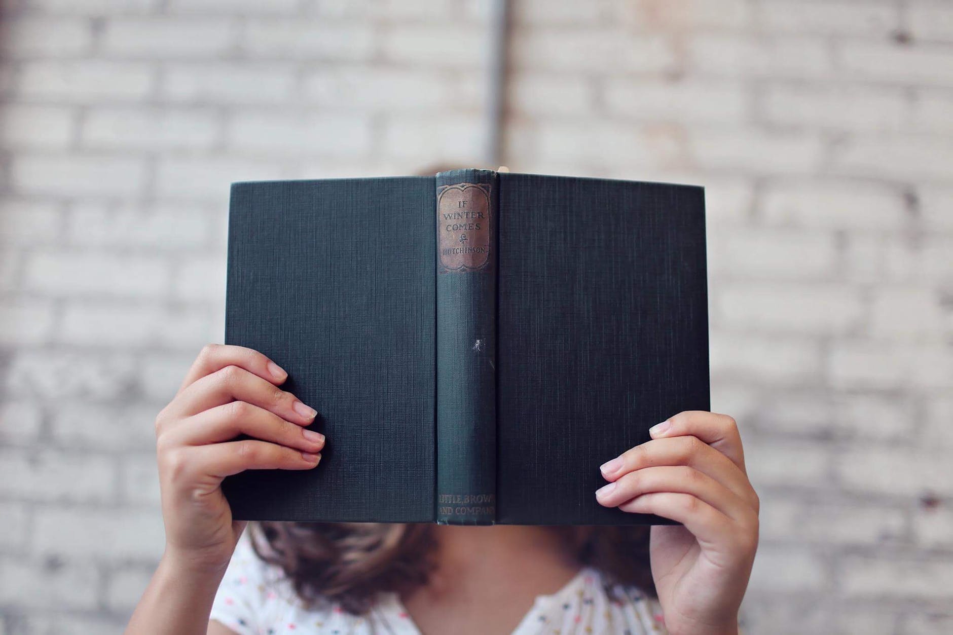 woman reading hard cover book with it covering her face