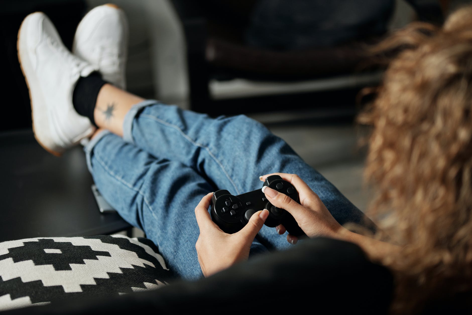 person with curly hair playing video games with legs up on ottoman