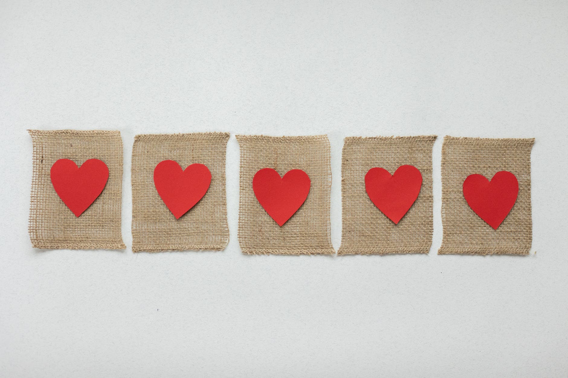 row of red paper hearts cut out and laid on burlap sheets on a white background